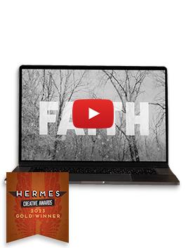A still from "Step Out in Faith" - The word "faith" in big bold white letters over an image of bare winter trees in the snow - on a black laptop with a Gold 2023 Hermes Award