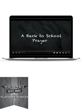 The white text "A Back to School Prayer" on a black screen on a black laptop with a Platinum 2022 Hermes Award